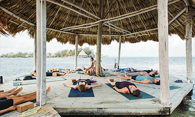 Retreat goers at Thatch Caye meditate on the overwater palapa _ Belize Retreats